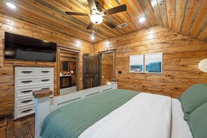 A wooden cabin room with a bed, a dresser, a ceiling fan, and a window with a view. - The Rustic Ritz|2BD 2BTH|Hot tub|Shuffleboard|Luxury|SLPs8 (Broken Bow)