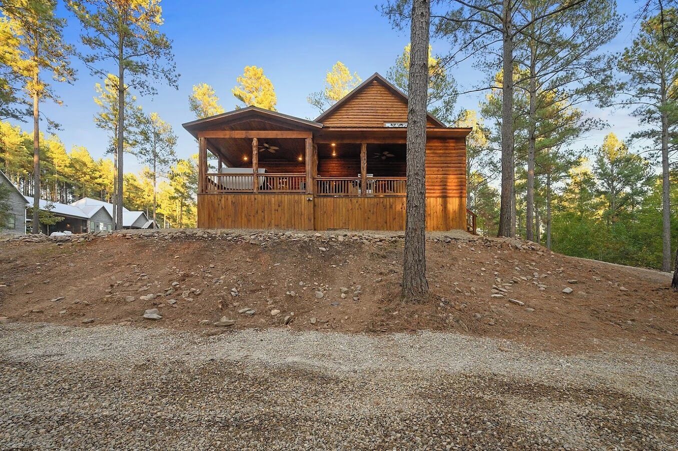 Une cabane en bois dotée d’un porche, entourée d’arbres et bordée d’un sentier de terre.
