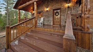 Eine Holzhütte mit Steinfassade, einer Veranda mit Holzgeländern und einem weißen Schaukelstuhl.
