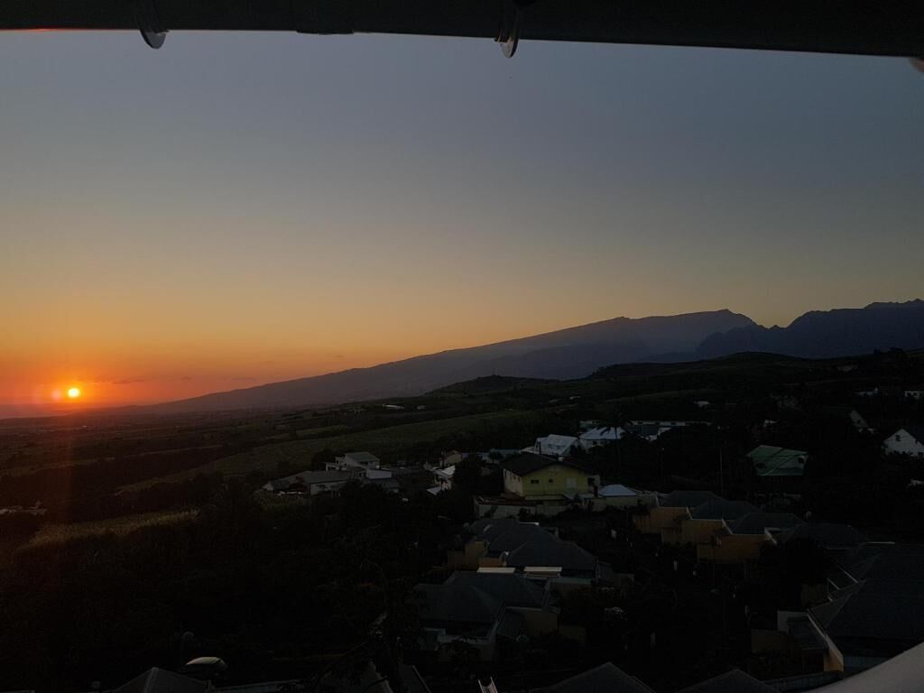 Un coucher de soleil sur une zone résidentielle, avec des maisons et des montagnes en arrière-plan.