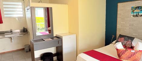 A compact room with a bed, a desk, a small refrigerator, a sink, and a window with curtains.