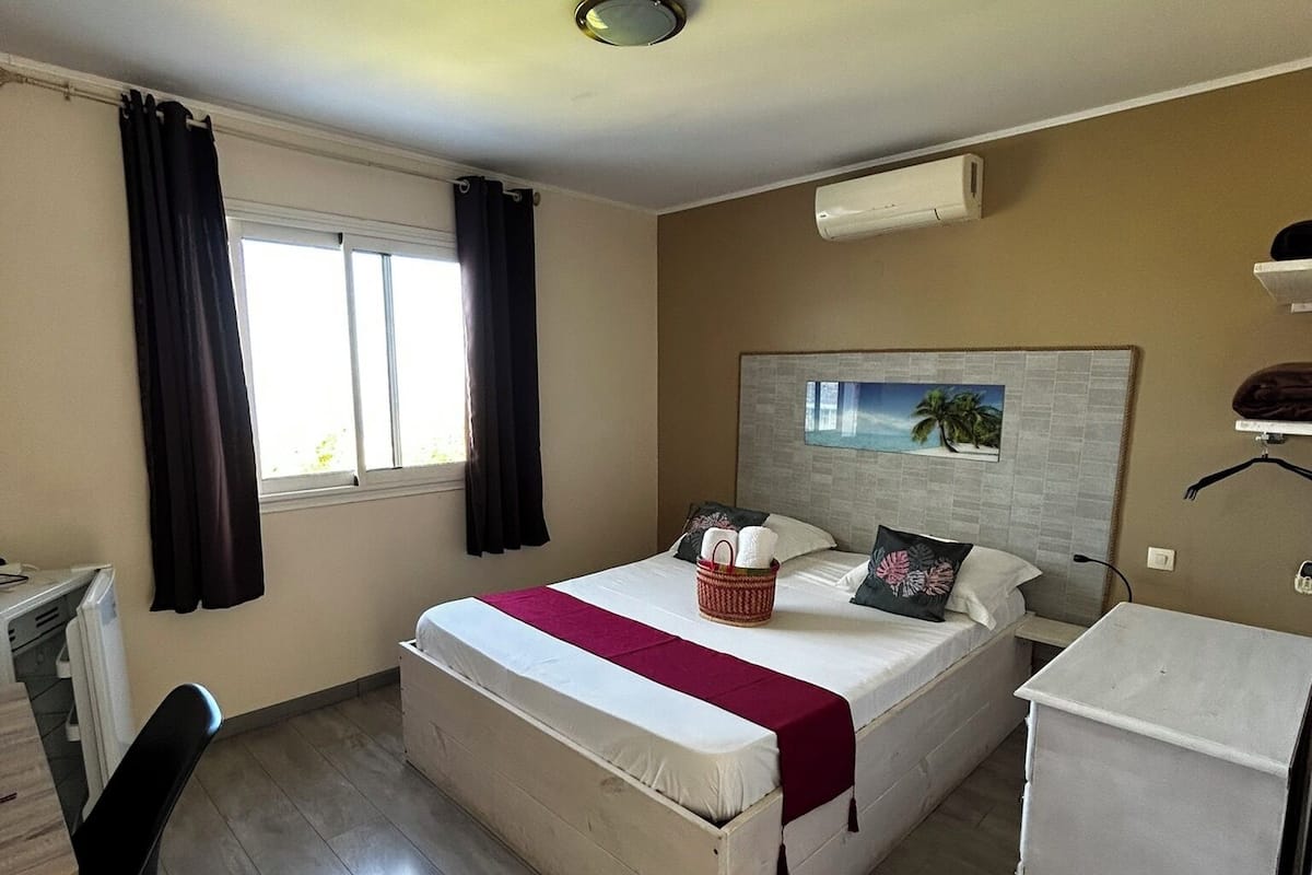 Habitación de hotel con cama, escritorio, silla, refrigerador pequeño y ventana con cortinas.