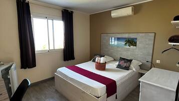 Habitación de hotel con cama, escritorio, silla, refrigerador pequeño y ventana con cortinas.