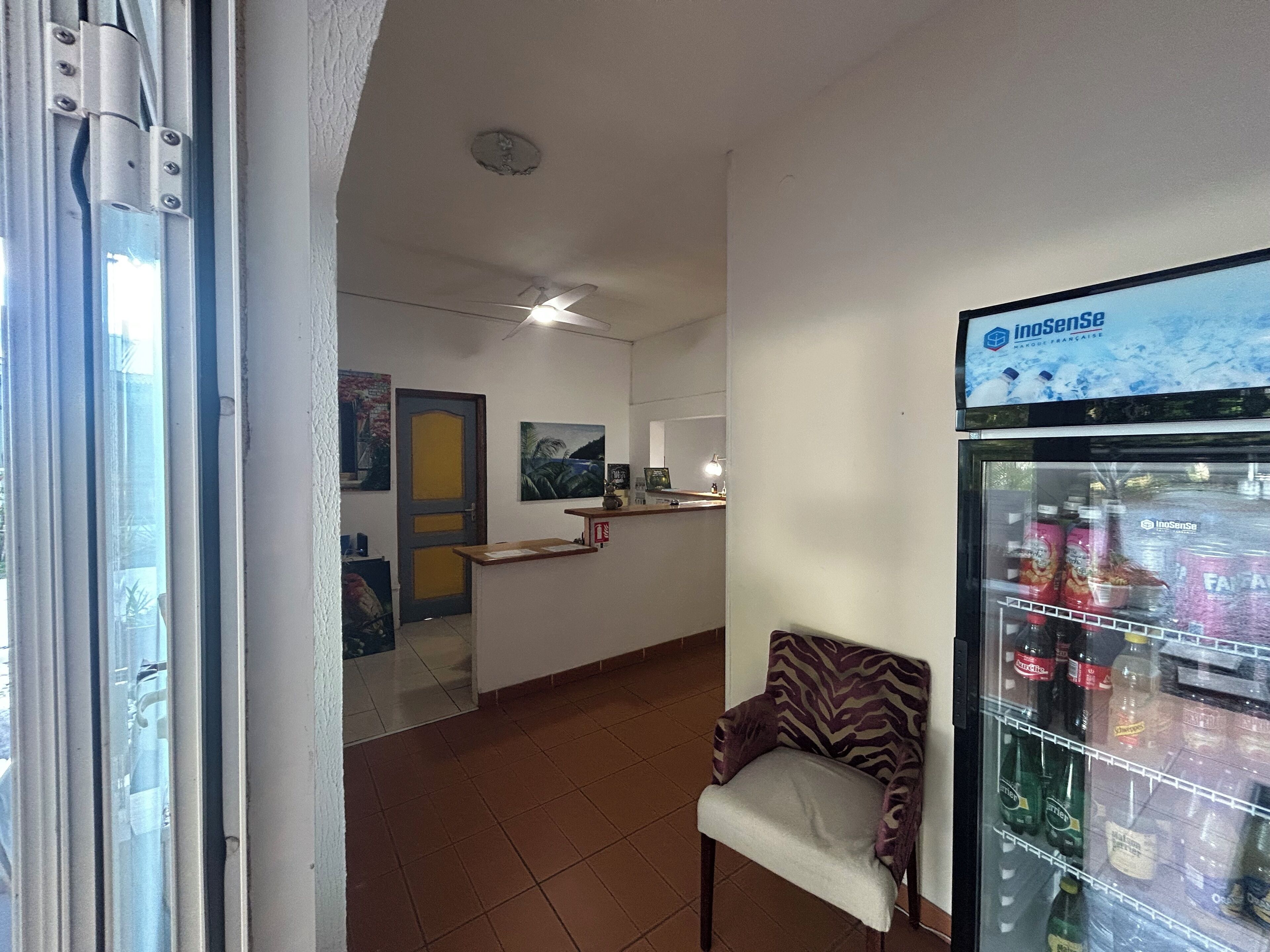 Un hall de hotel con una recepción, una silla, un refrigerador lleno de bebidas y obras de arte en las paredes.