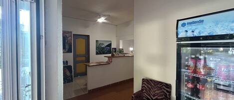 Un hall de hotel con una recepción, una silla, un refrigerador lleno de bebidas y obras de arte en las paredes.