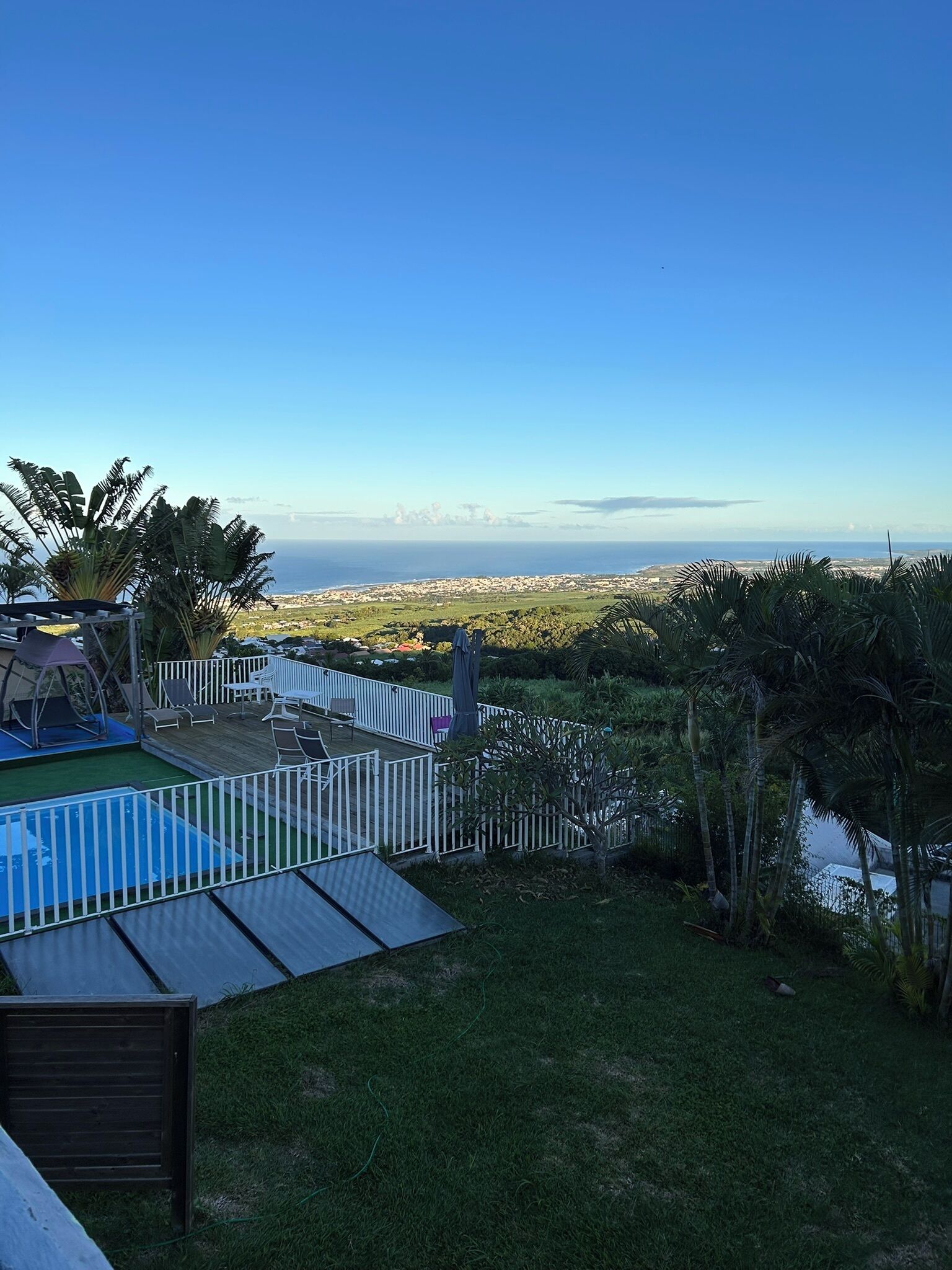 A backyard with a swimming pool, a fenced patio area, and a view of the ocean.