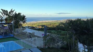 A backyard with a swimming pool, a fenced patio area, and a view of the ocean.