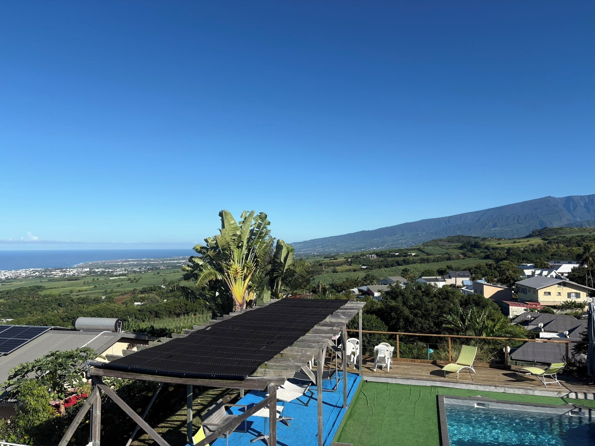 A rooftop pool with solar panels, a view of the ocean, and a mountainous landscape.