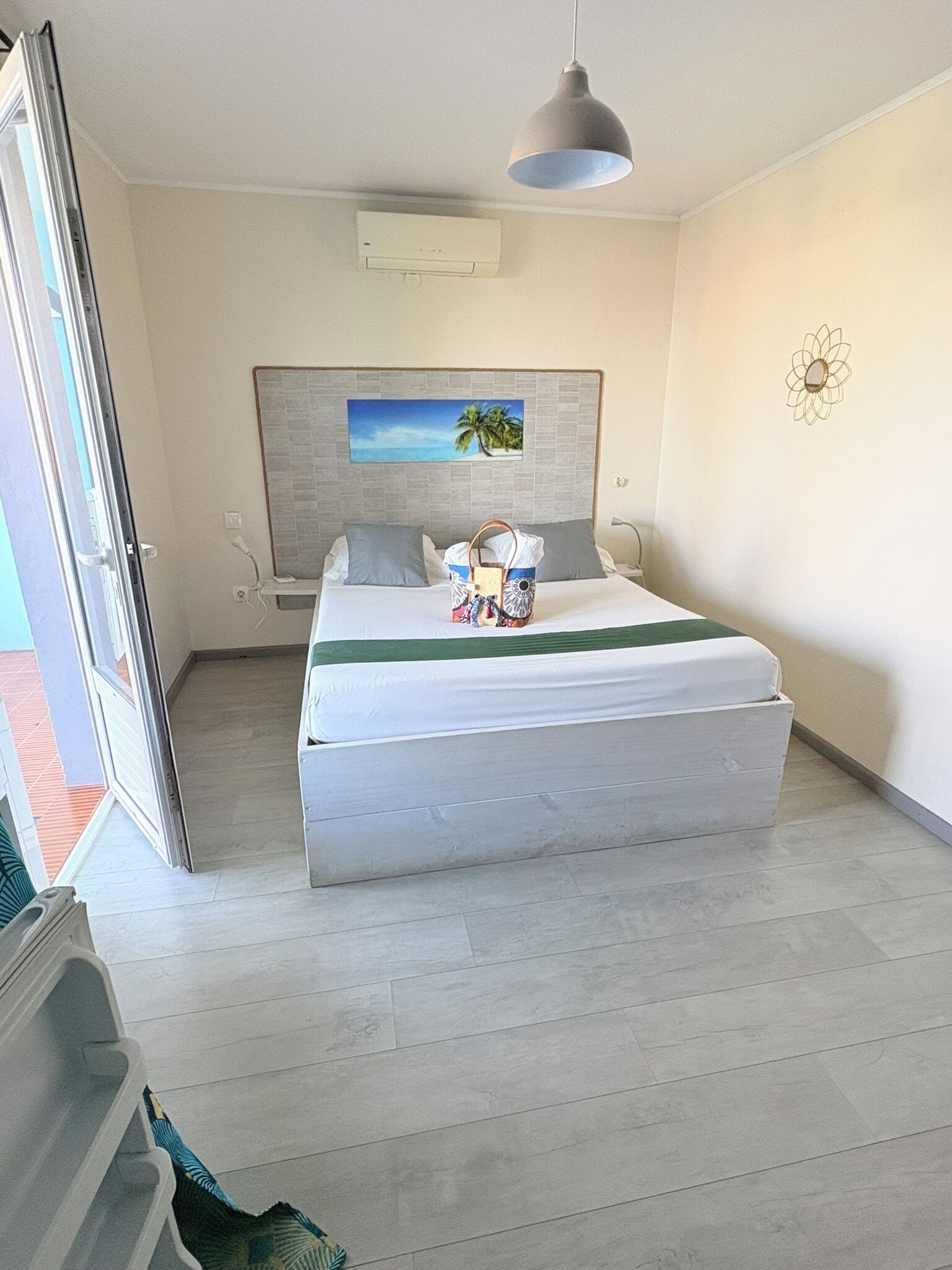 Ein Hotelzimmer mit Bett, einem Gemälde an der Wand, einer Deckenleuchte und einem Fenster.