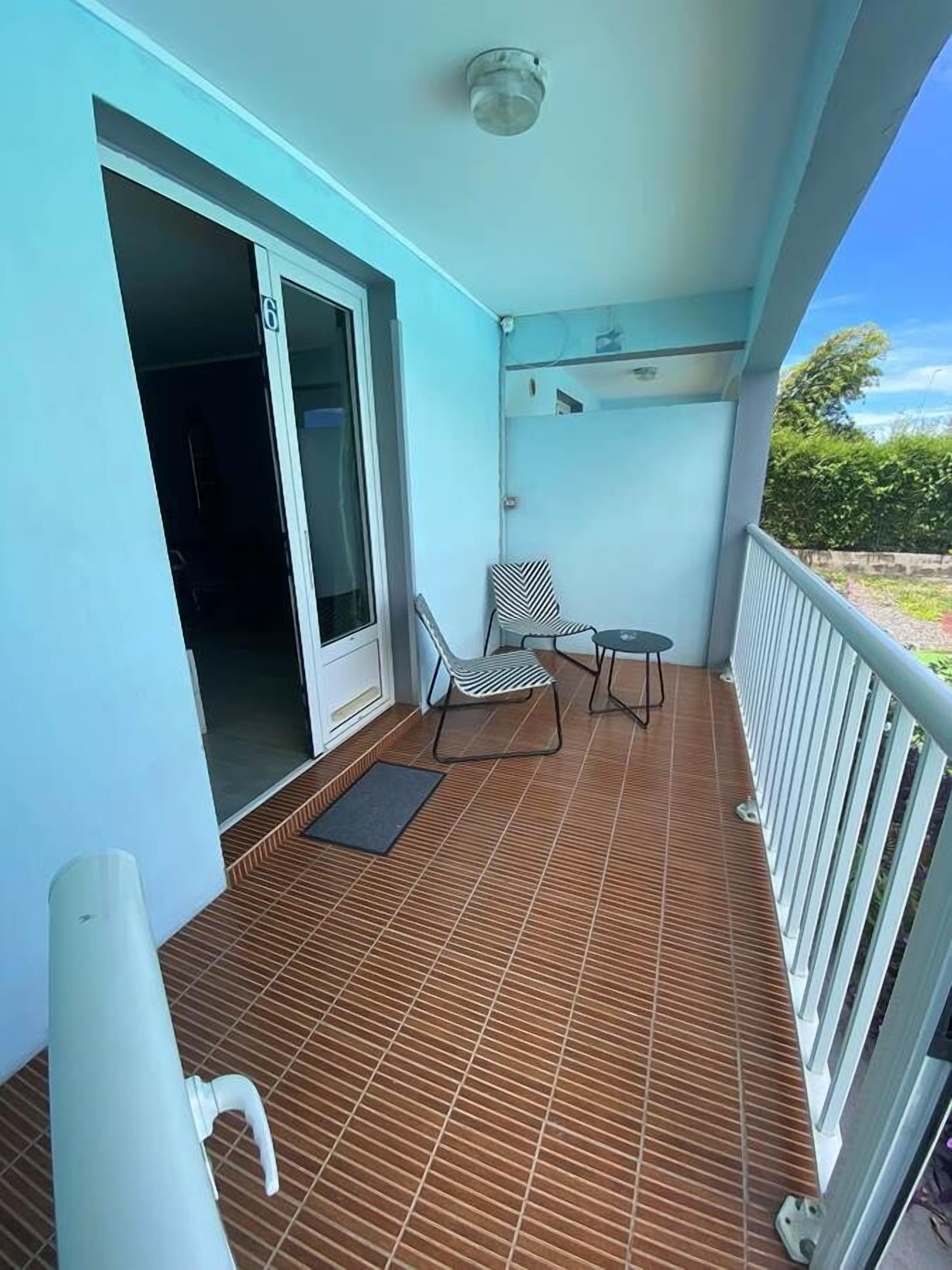 A balcony with a tiled floor, a chair, a small table, and a door leading to an interior space.