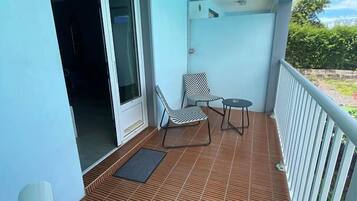A balcony with a tiled floor, a chair, a small table, and a door leading to an interior space.