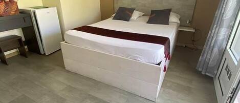 Una camera da letto con un letto grande, una scrivania, un piccolo frigorifero e una finestra con tende.