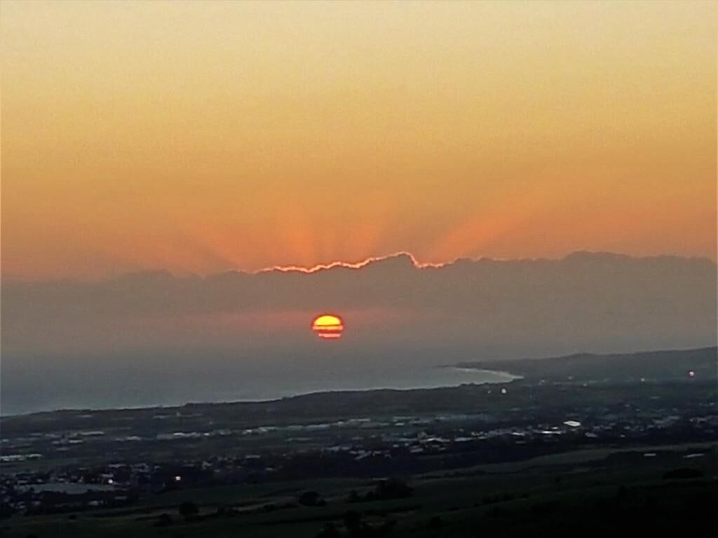 Un atardecer sobre un paisaje costero con una línea de horizonte visible y un pueblo en primer plano.