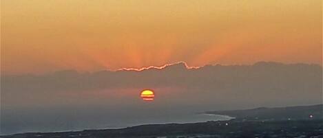 Un atardecer sobre un paisaje costero con una línea de horizonte visible y un pueblo en primer plano.