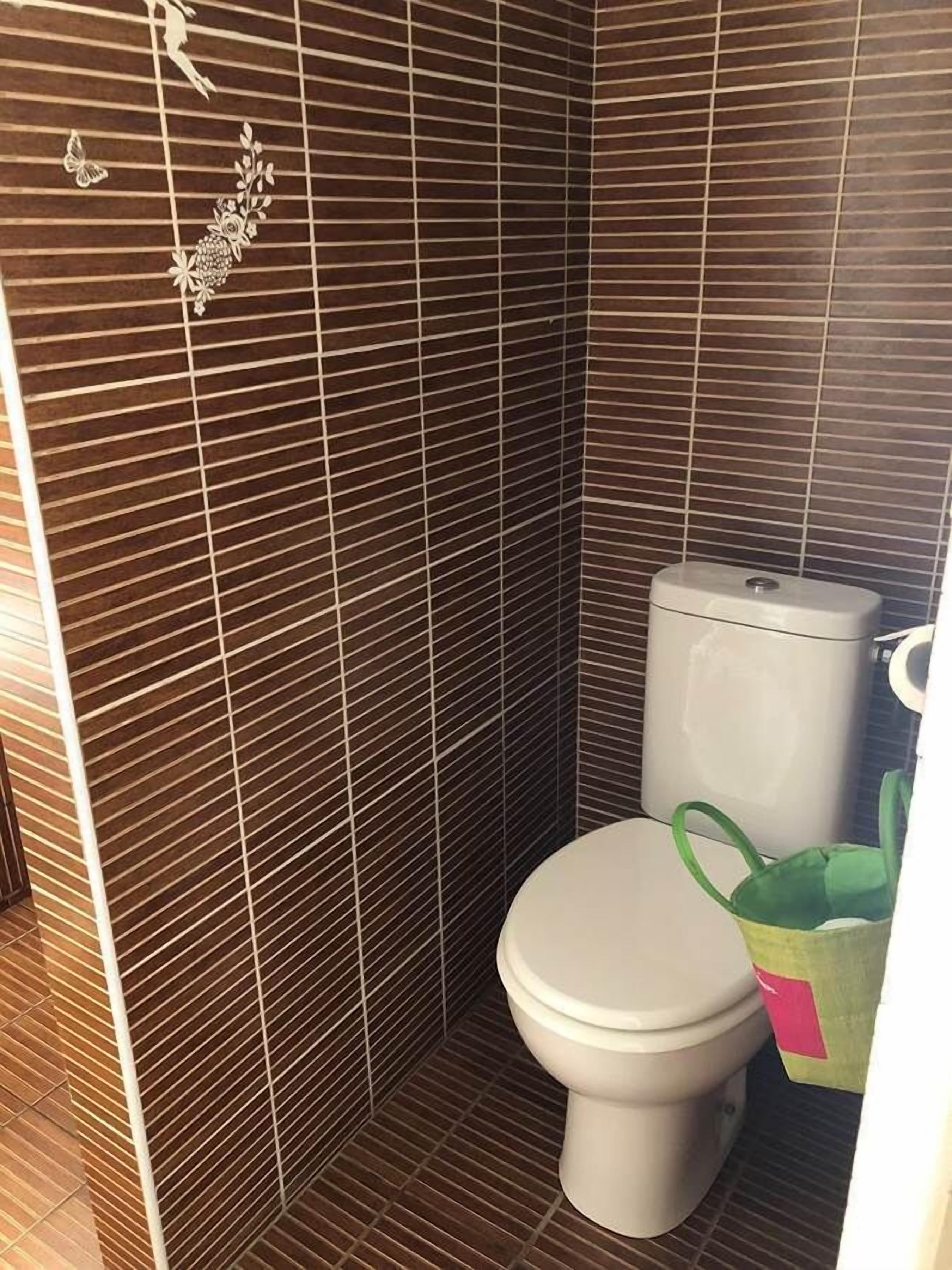 Un baño con inodoro, zona de ducha y pared de azulejos con un diseño decorativo.