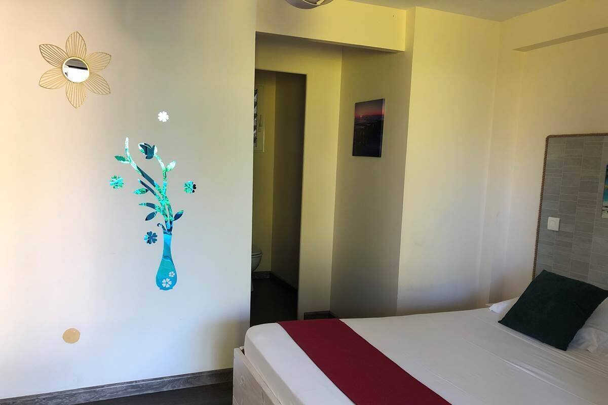 Habitación de hotel con cama, una manta roja, espejo montado en la pared y un adhesivo mural con un jarrón y flores.