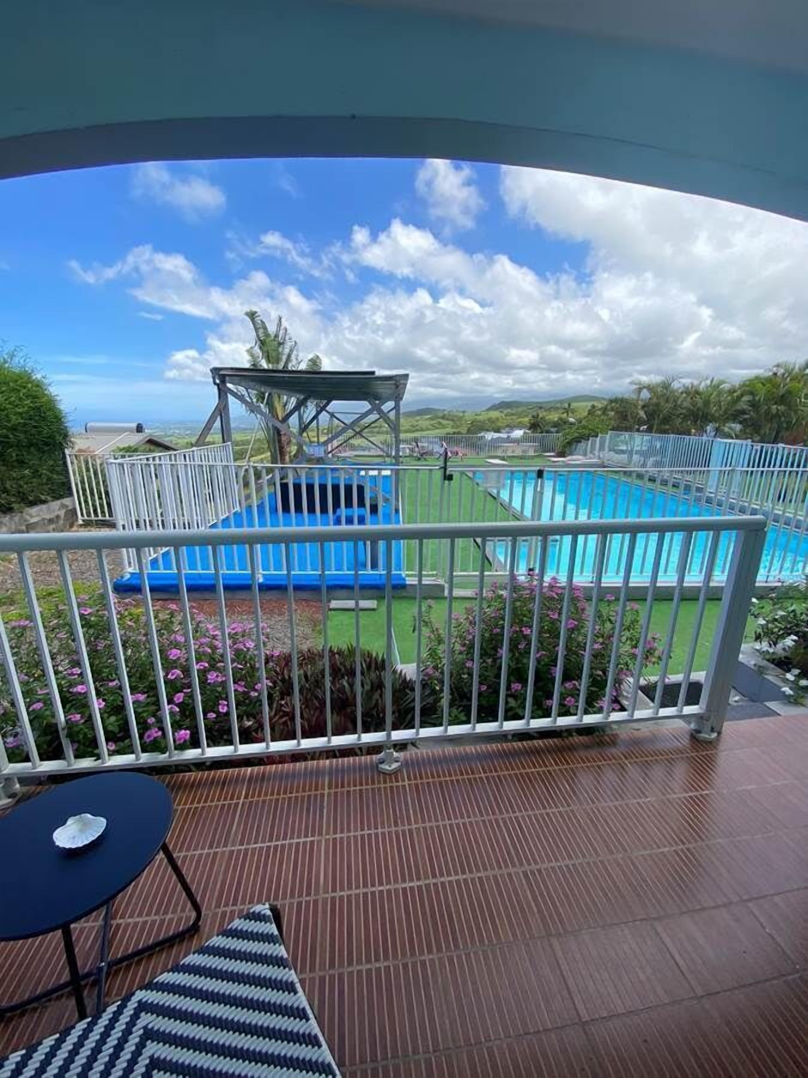 Un balcón con vistas a una piscina, un espacio de estar cubierto y un jardín con flores.