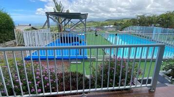Un balcón con vistas a una piscina, un espacio de estar cubierto y un jardín con flores.