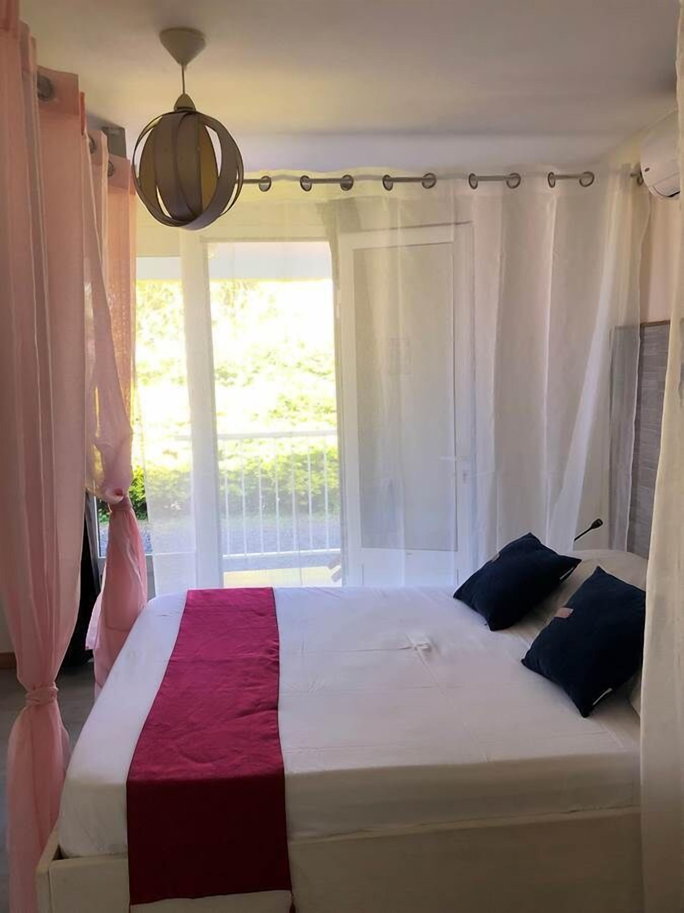 A bedroom with a bed, a red blanket, and a ceiling light.