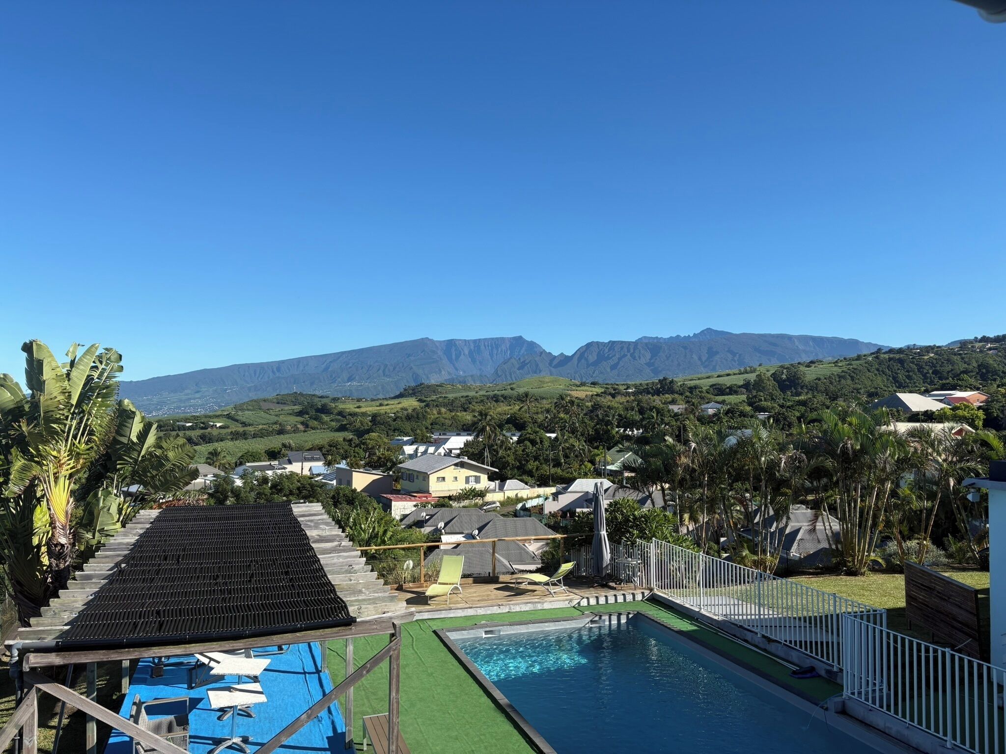 Zona de piscina con vistas a las montañas, rodeada de casas y vegetación.