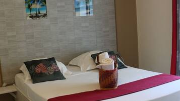 Habitación de hotel con una cama grande, cabecera con obra de arte, manta roja y una cesta tejida con una toalla.