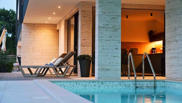 Un área de piscina moderna al aire libre con sillones de descanso y un bar.
