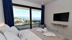 A hotel room with a bed, a TV mounted on the wall, and a view of the city and sea through large windows. - Beautiful Villa near centar of town for 4 person B (Icici)