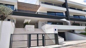 A modern multi-story building with a prominent staircase leading to the entrance, a gated driveway, and a minimalist architectural design. - Beautiful Villa near centar of town for 4 person B (Icici)