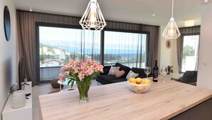 A modern living room with a large window, a wooden dining table, a vase of flowers, and a bowl of lemons. - Beautiful Villa near centar of town for 4 person B (Icici)