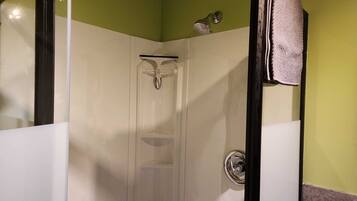 A glass-enclosed shower stall with a chrome faucet and showerhead, a towel hanging on the wall, and a visible toilet paper holder.