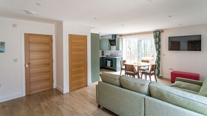 A modern living room with a green sofa, wooden doors, and a kitchen area with a dining table and chairs.