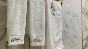 Un baño con pared de mármol, un perchero dorado con tres toallas y un dispensador de papel higiénico dorado.