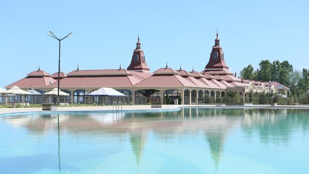 Una gran piscina con un edificio que presenta dos torres destacadas y un paseo cubierto.