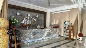 Un vestíbulo con un mostrador de recepción de mármol, maquetas de barcos y una escalera con barandilla.