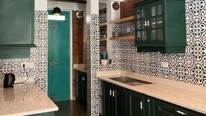 A kitchen with teal cabinets, patterned backsplash, and a hanging pendant light. - Tentgram Brick House (Kozhikode)