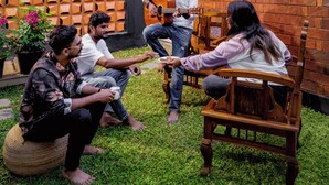A group of people sitting on a grassy lawn in front of a building with a brick facade and a geometric wall design. - Tentgram Brick House (Kozhikode)