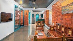 A hallway with wooden benches, a ceiling fan, and a brick wall with a mural. - Tentgram Brick House (Kozhikode)