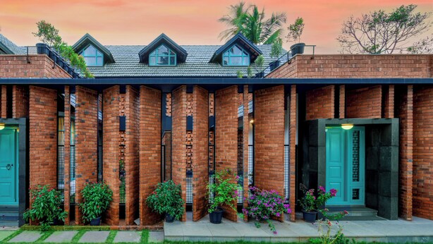 A brick building with a green door, a balcony, and potted plants. - Tentgram Brick House (Kozhikode)