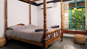 A four-poster bed with a wooden frame and a grey bedspread, a window with green shutters, and a ceiling fan. - Tentgram Brick House (Kozhikode)