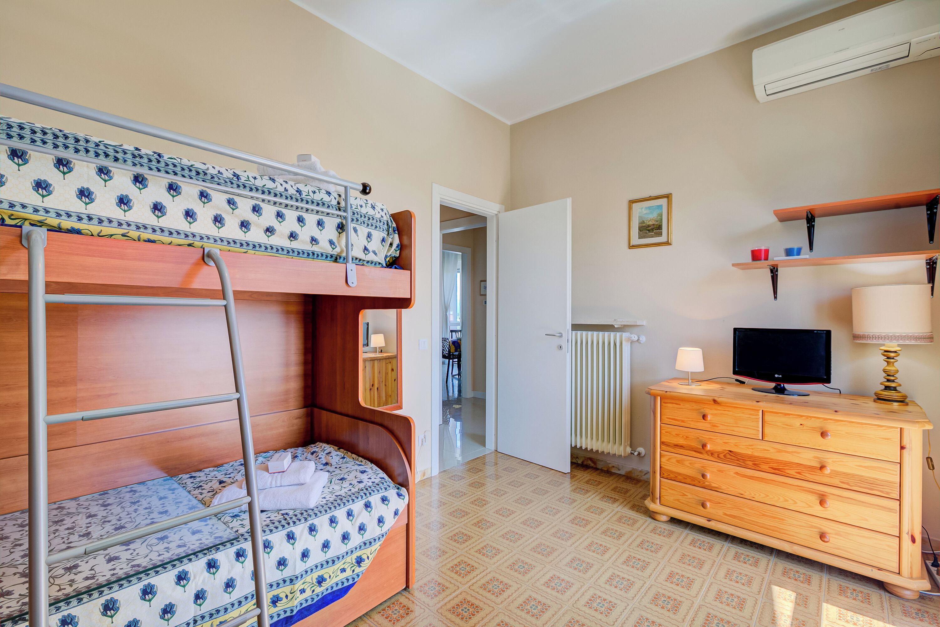 Ein Zimmer mit einem Etagenbett, einem Holzkasten, einem Fernseher und einer Heizung.