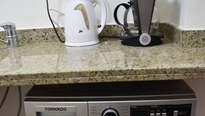 Eine kompakte Waschmaschine und Trockner-Kombination mit Bedienfeld, einem Wasserkocher und einer Kaffeemaschine auf der Arbeitsplatte.