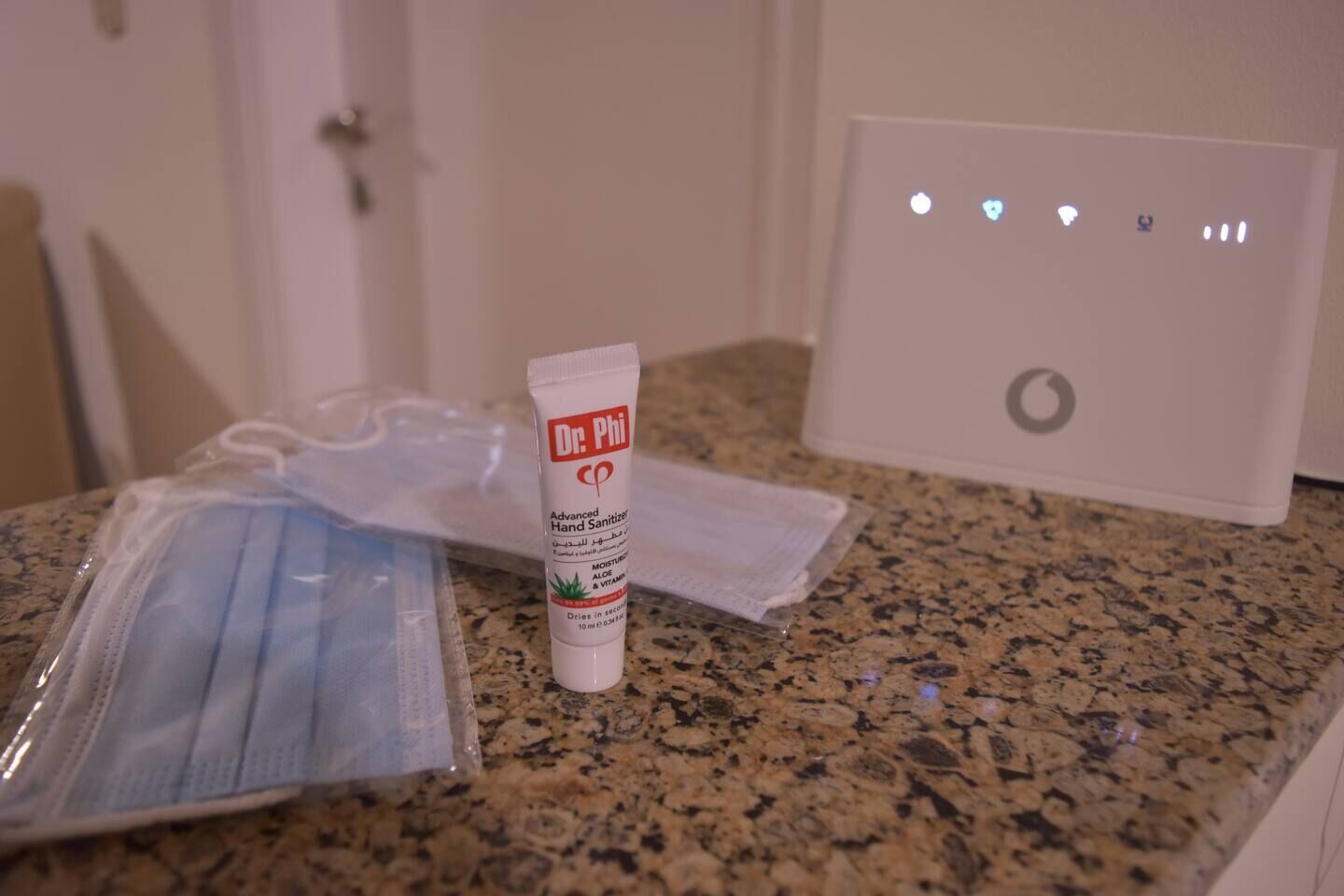 A countertop with a tube of Dr. Phi hand sanitizer, a package of face masks, and a white device with a circular logo.
