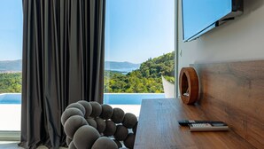 A room with a large window, a wooden table, a remote control, and a wall-mounted TV. - Luxury Villa Morello Korcula 1 with Heated Pool (Korcula)