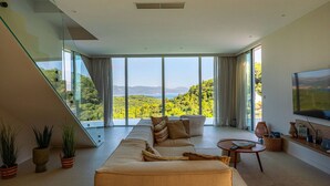 Una sala de estar moderna con un sofá grande, un televisor y vistas a un paisaje montañoso.