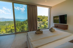 Quarto com uma janela ampla, televisão de tela plana e toalhas dobradas na cama.