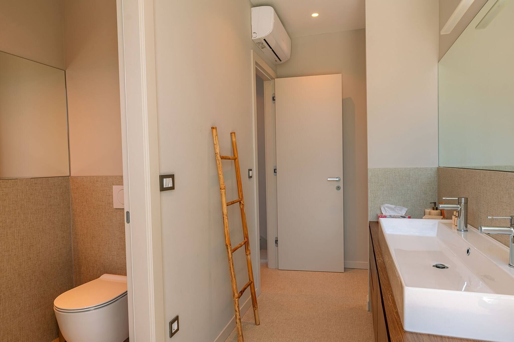 Et badeværelse med toilet, håndvask, spejl og en klimaanlæg.