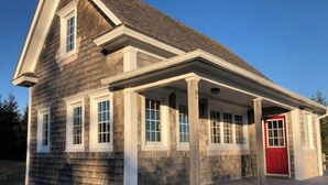 A two-story house with a porch, a red door, and a chimney. - Beautiful oceanfront cottage (Guysborough)