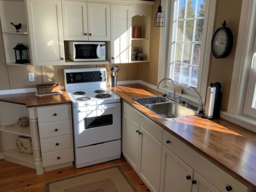 A kitchen with white cabinets, a stove, a microwave, and a sink.