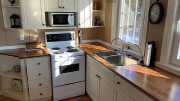 A kitchen with white cabinets, a stove, a microwave, and a sink.