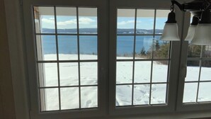 A room with a large window overlooking a snowy landscape and a body of water. - Beautiful oceanfront cottage (Guysborough)